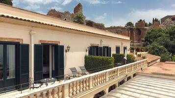 Un hotel con balcón, mobiliario exterior y vistas a ruinas antiguas.
