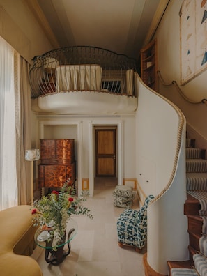 A spacious living area with a curved staircase, a piano, and a small table with flowers.