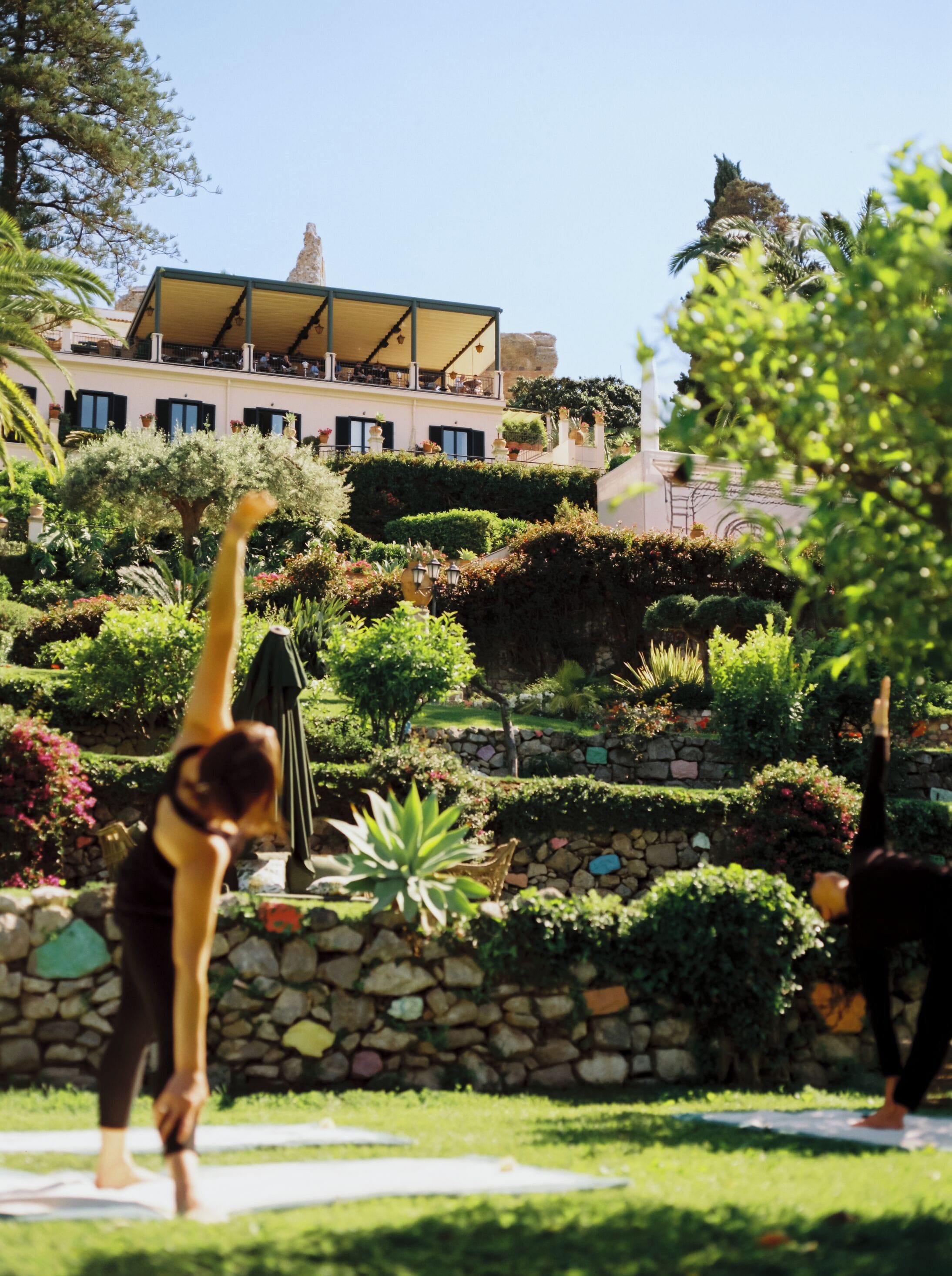 Una persona practicando yoga en un jardín con un edificio al fondo.