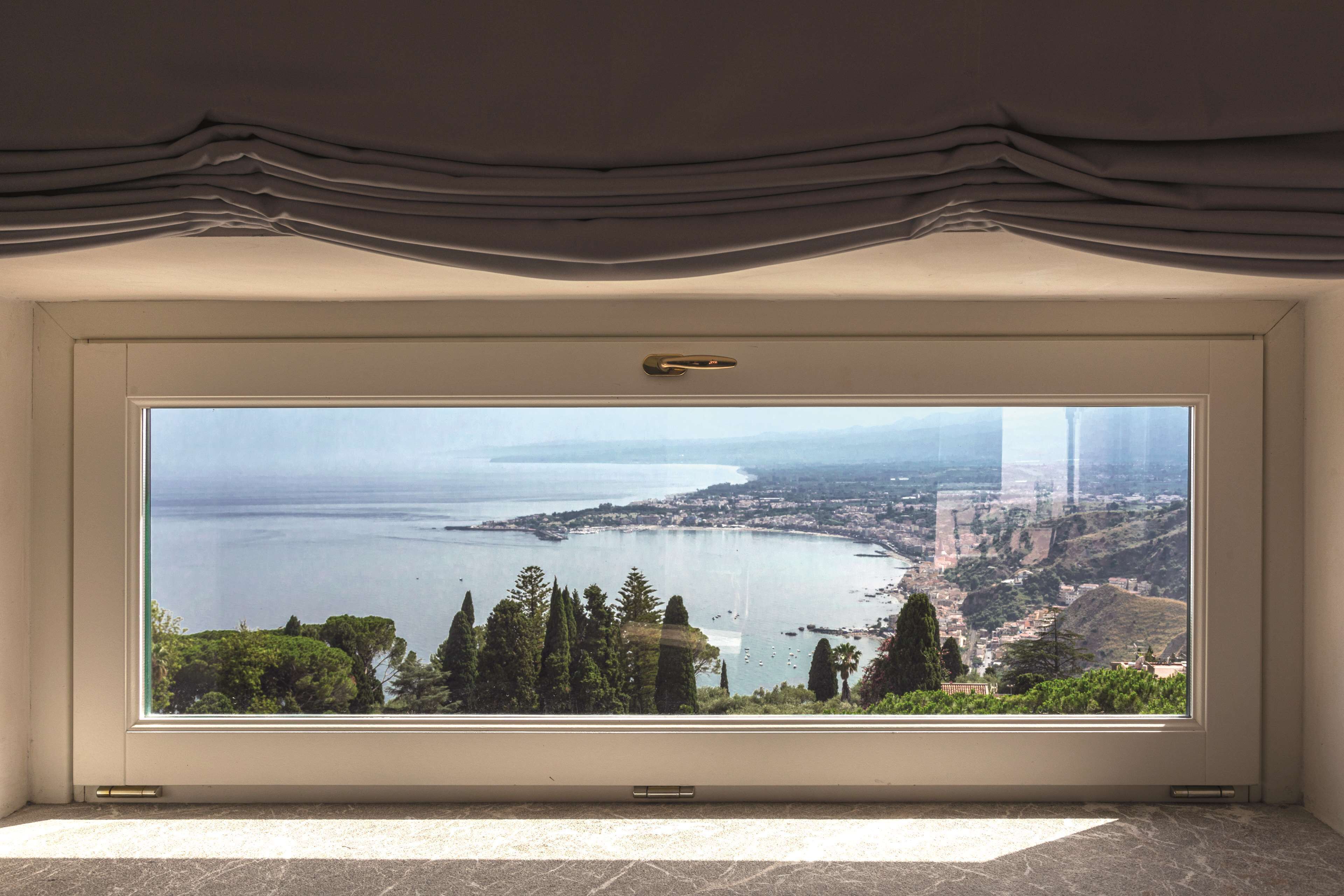 Una habitación con un amplio ventanal que ofrece vistas a un paisaje costero, una puerta con manija y un piso de baldosas.