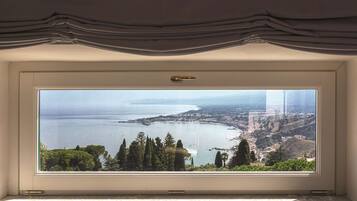 Una habitación con un amplio ventanal que ofrece vistas a un paisaje costero, una puerta con manija y un piso de baldosas.