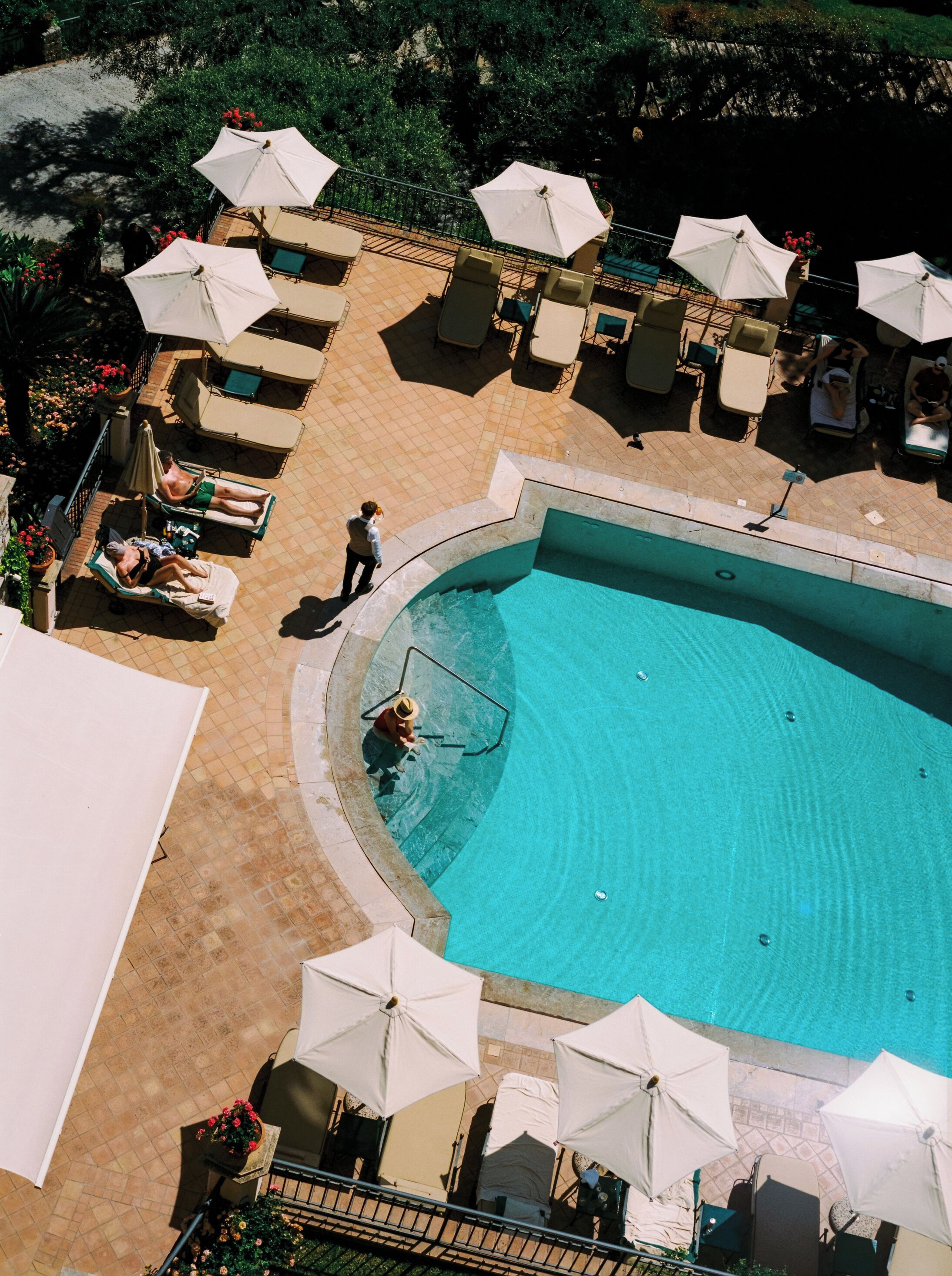 Vista aérea de uma área de piscina com espreguiçadeiras e guarda-sóis.