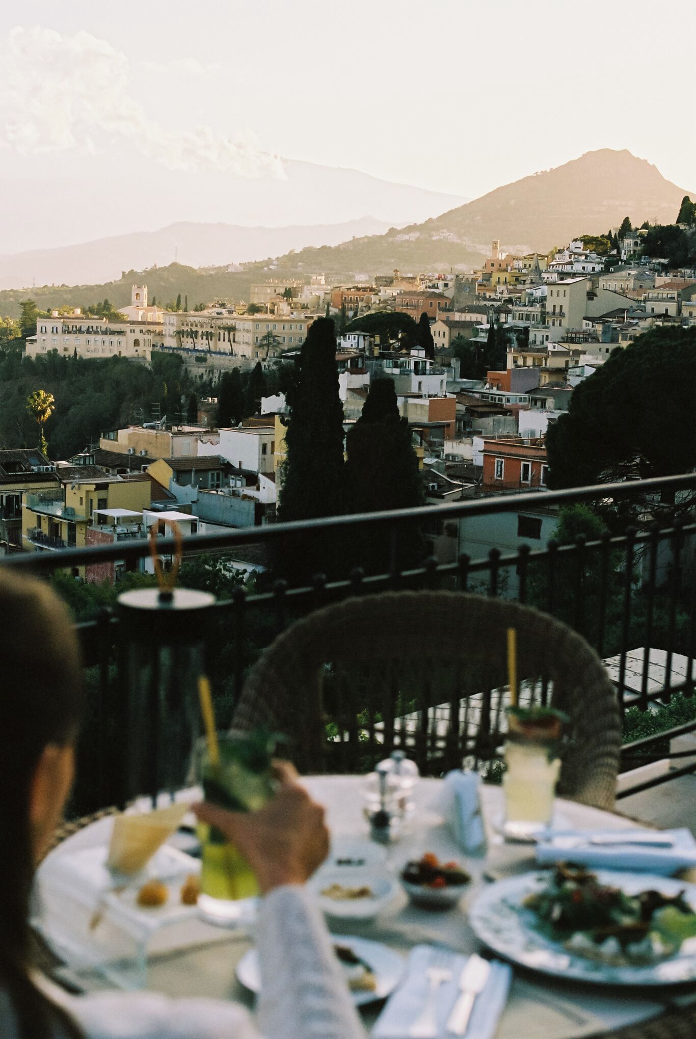 Una mesa de comedor con platos y cubiertos, con vistas a un paisaje urbano con edificios y una montaña al fondo.