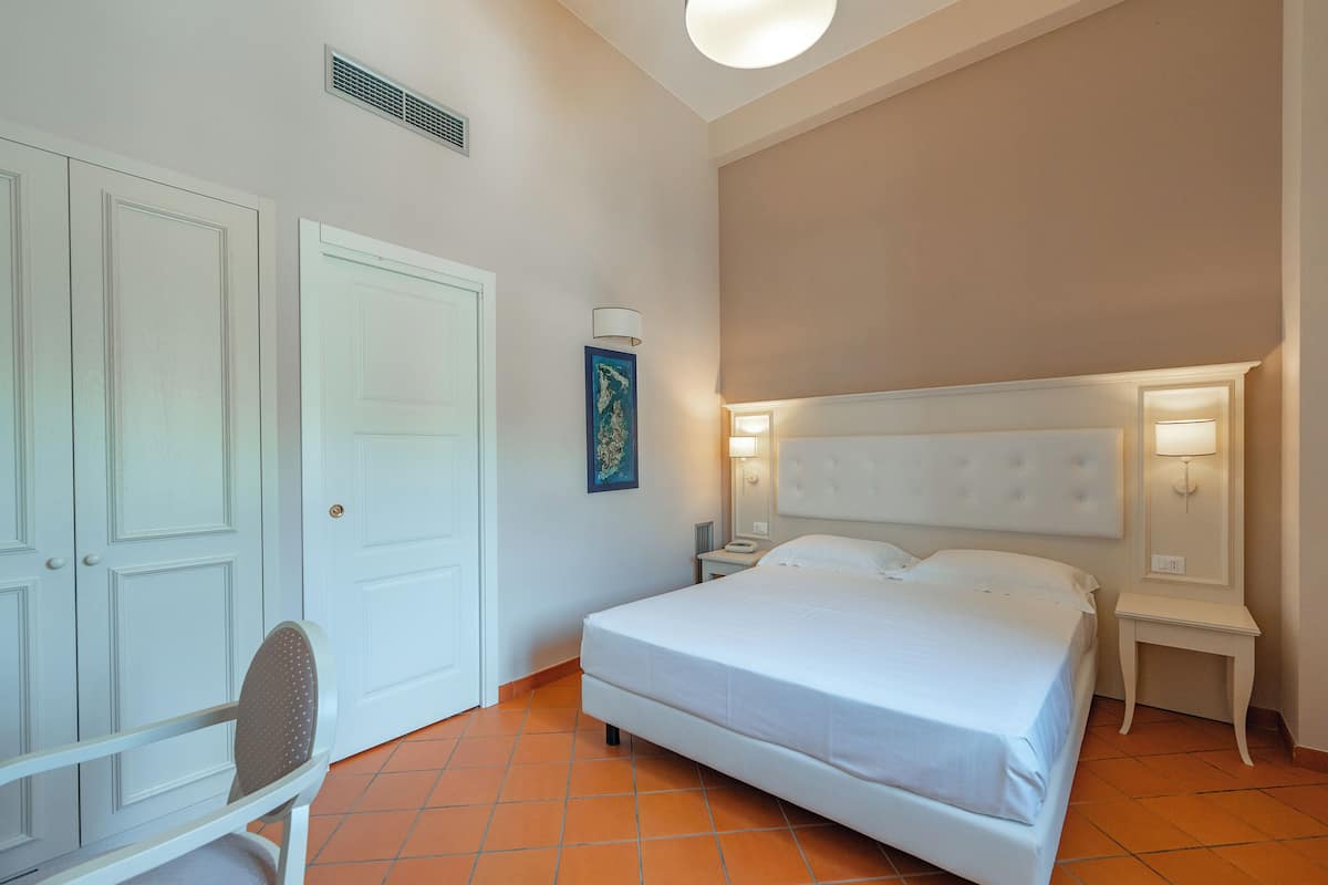 Une chambre à coucher comprenant un lit, une chaise, une table de chevet et une lampe fixée au mur.