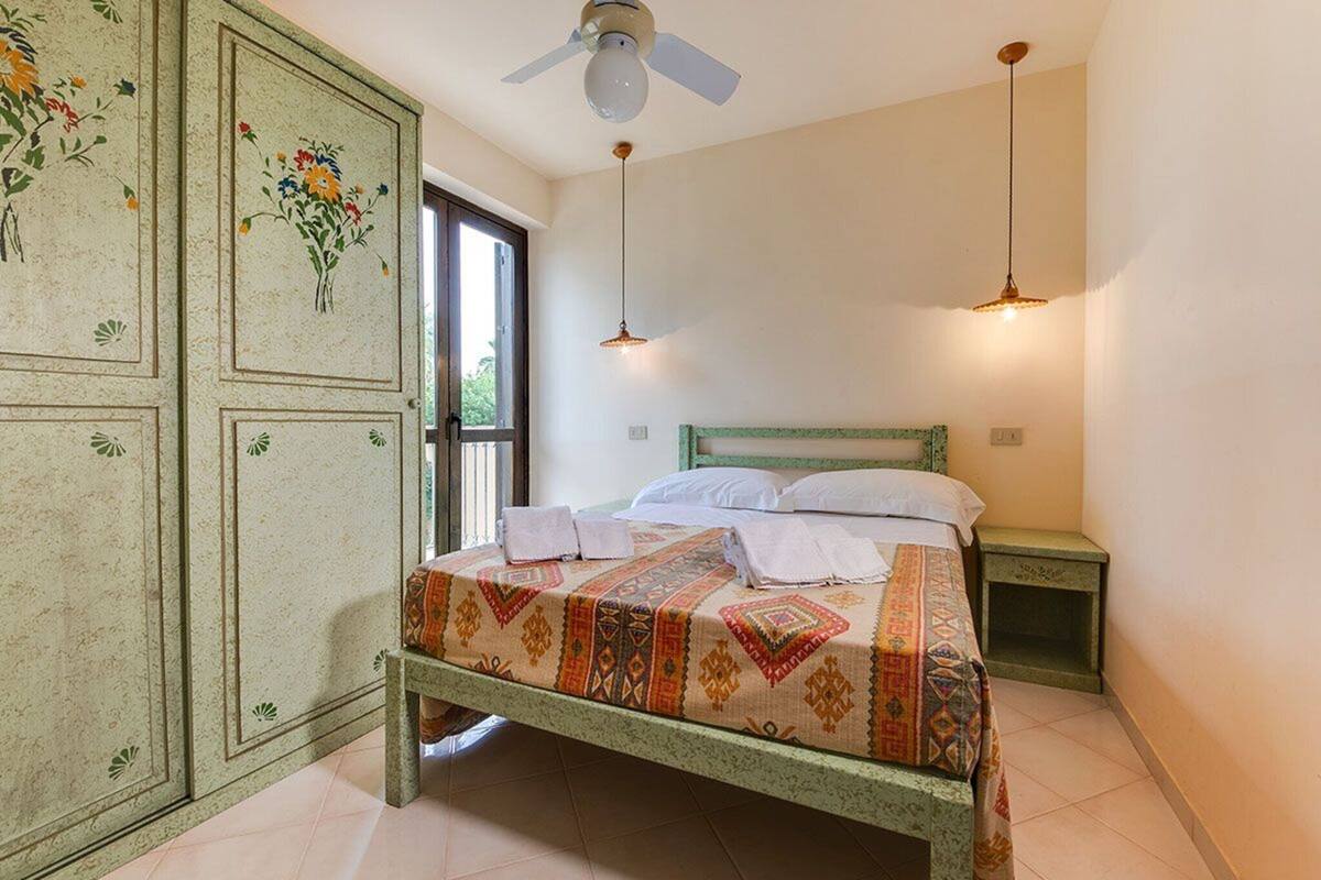 Une chambre à coucher comprenant un lit, une table de chevet, une armoire et un ventilateur de plafond.
