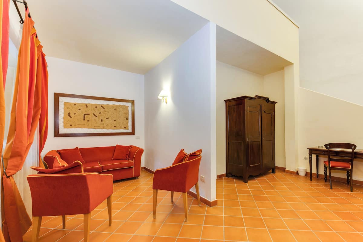 Un salon avec un canapé rouge, deux fauteuils rouges, un meuble en bois et une œuvre d’art abstraite encadrée accrochée au mur.