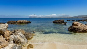 Una playa rocosa con aguas transparentes y montañas a lo lejos.
