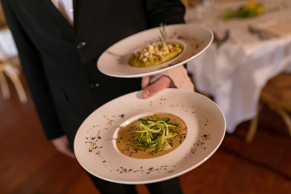 A person holding two plates of food, one with a green dish and the other with a brown dish, in a restaurant setting.