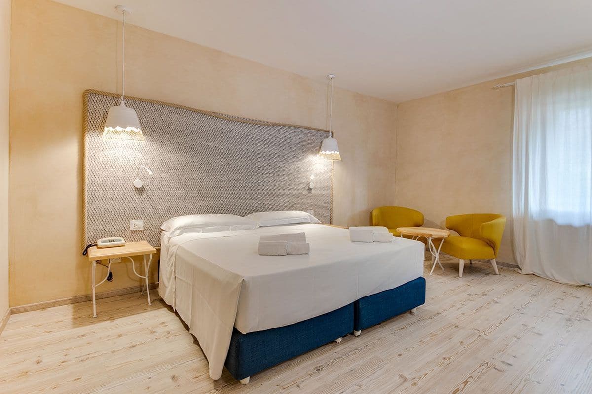 Une chambre d’hôtel moderne avec un grand lit, des tables de chevet, un petit bureau et deux chaises jaunes.