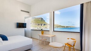 Habitación de hotel con cama, televisión, escritorio con silla y vista al mar y acantilados.