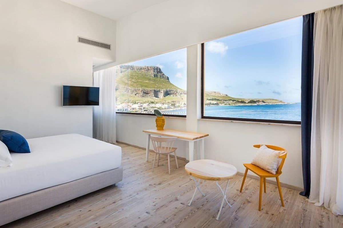 Une chambre d’hôtel avec un lit, une télévision, un bureau avec une chaise et une vue sur la mer et les falaises.
