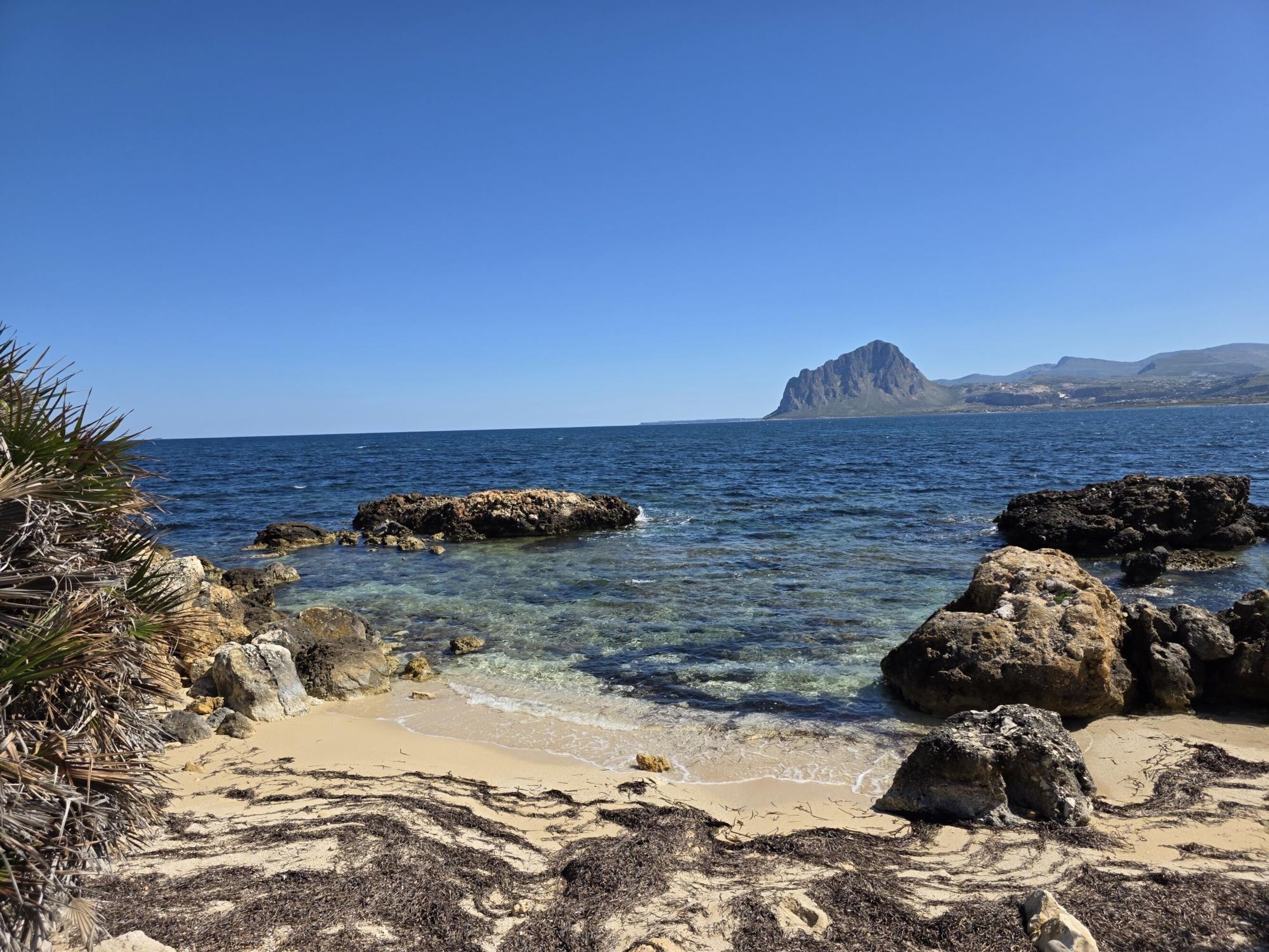 Una spiaggia con acqua cristallina, scogliere rocciose e una montagna in lontananza.
