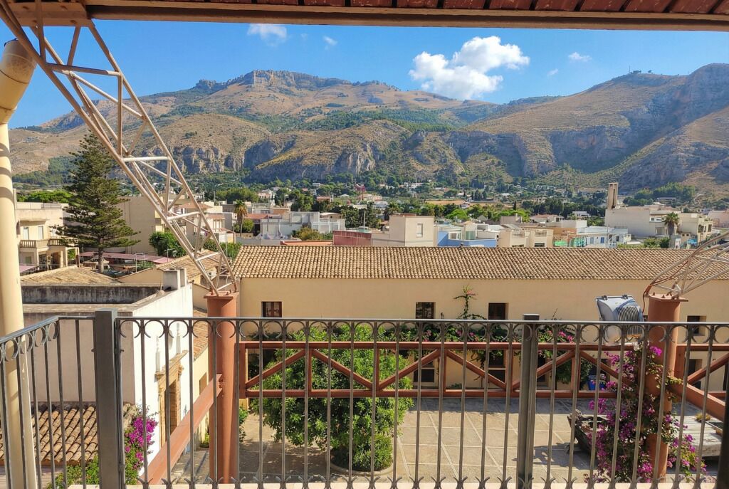 A balcony with a metal railing overlooking a town with buildings and mountains in the background.
