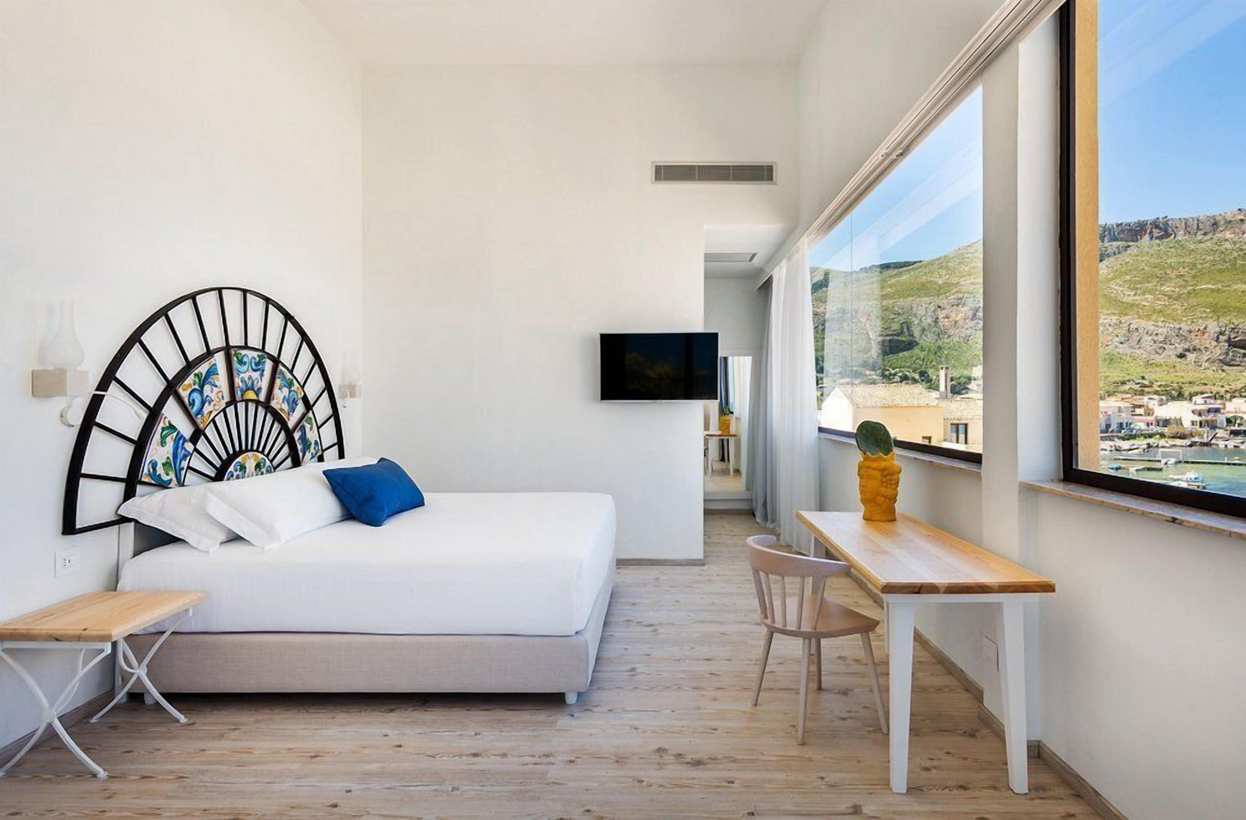 Un dormitorio moderno con cama, escritorio y silla. Hay un televisor montado en la pared y una ventana con vistas al paisaje.