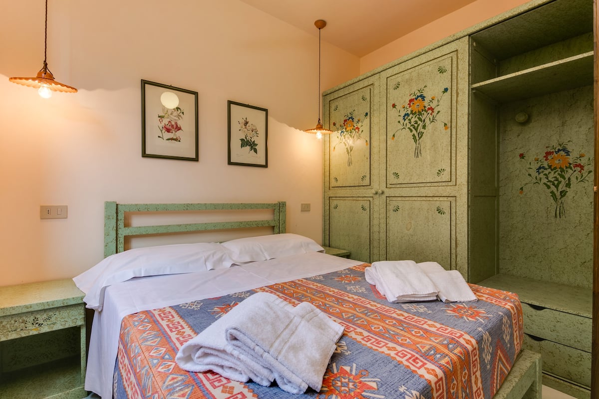 Un lit bien fait, avec une couvre-lit à motifs, une pile de serviettes pliées et une tête de lit en bois vert.