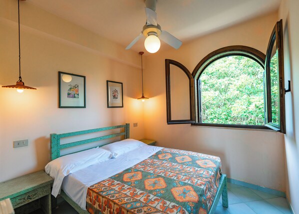 Quarto com cama, ventilador de teto, janela com persiana aberta e duas luzes de parede.
