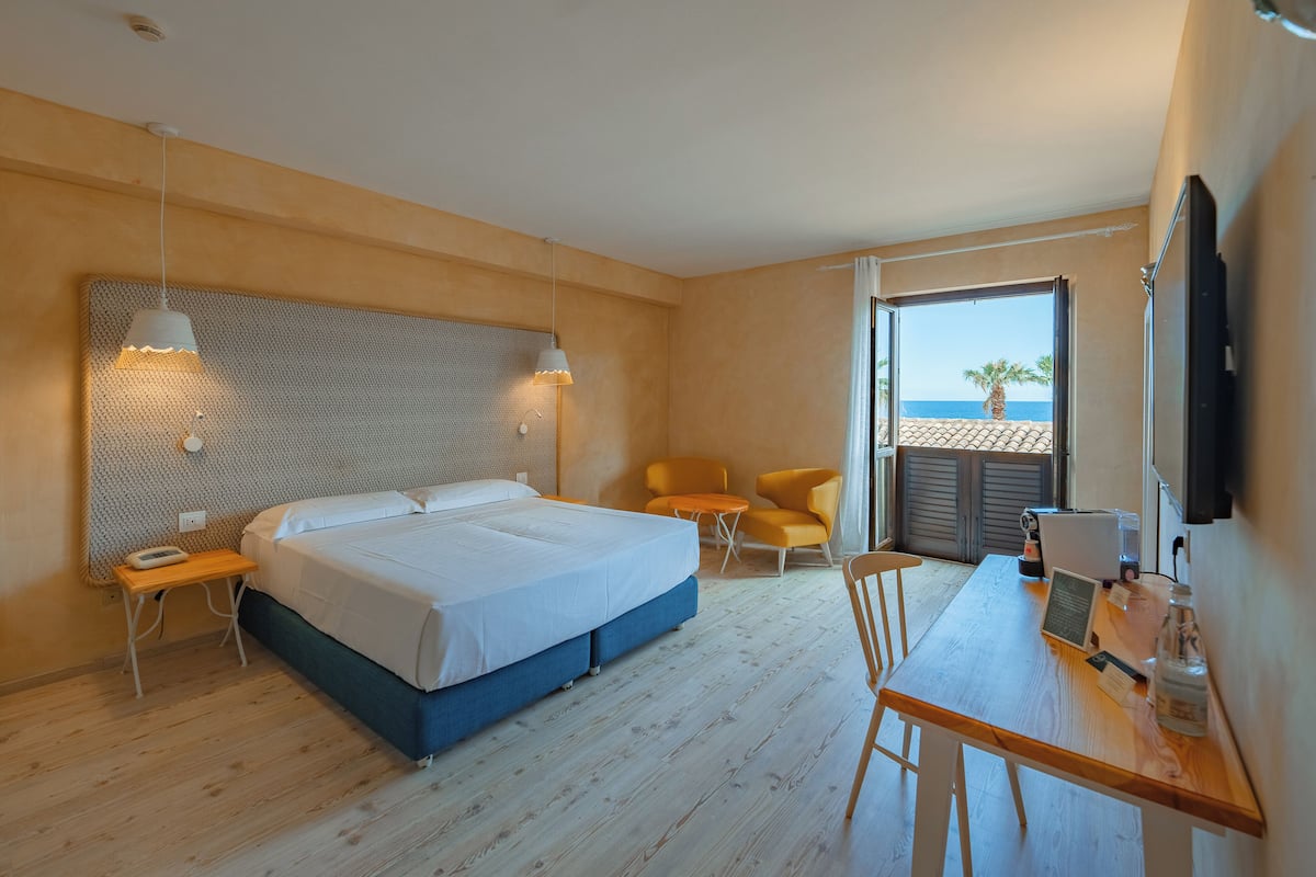 Une chambre d’hôtel comprenant un lit, un bureau avec une chaise, une petite table, un téléviseur et une vue sur la plage.