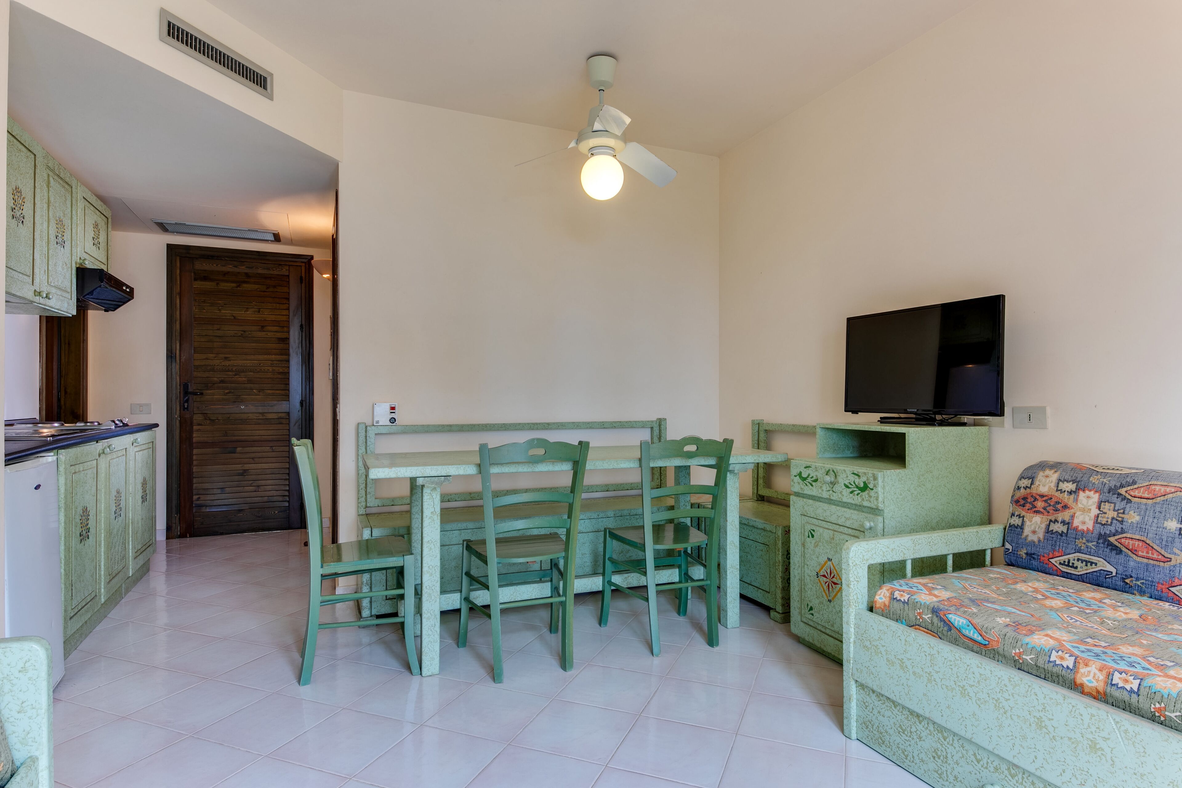 A compact living space with a dining area, a sofa, a television, and a kitchen area.
