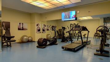 A gym with exercise equipment, a television, and posters on the walls.