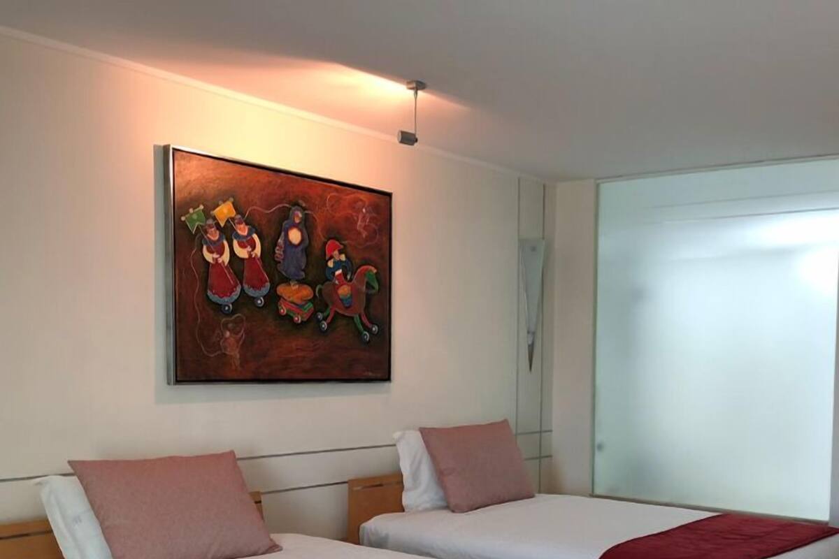 Habitación de hotel con dos camas, cada una con una manta roja, un cuadro en la pared y una ventana.