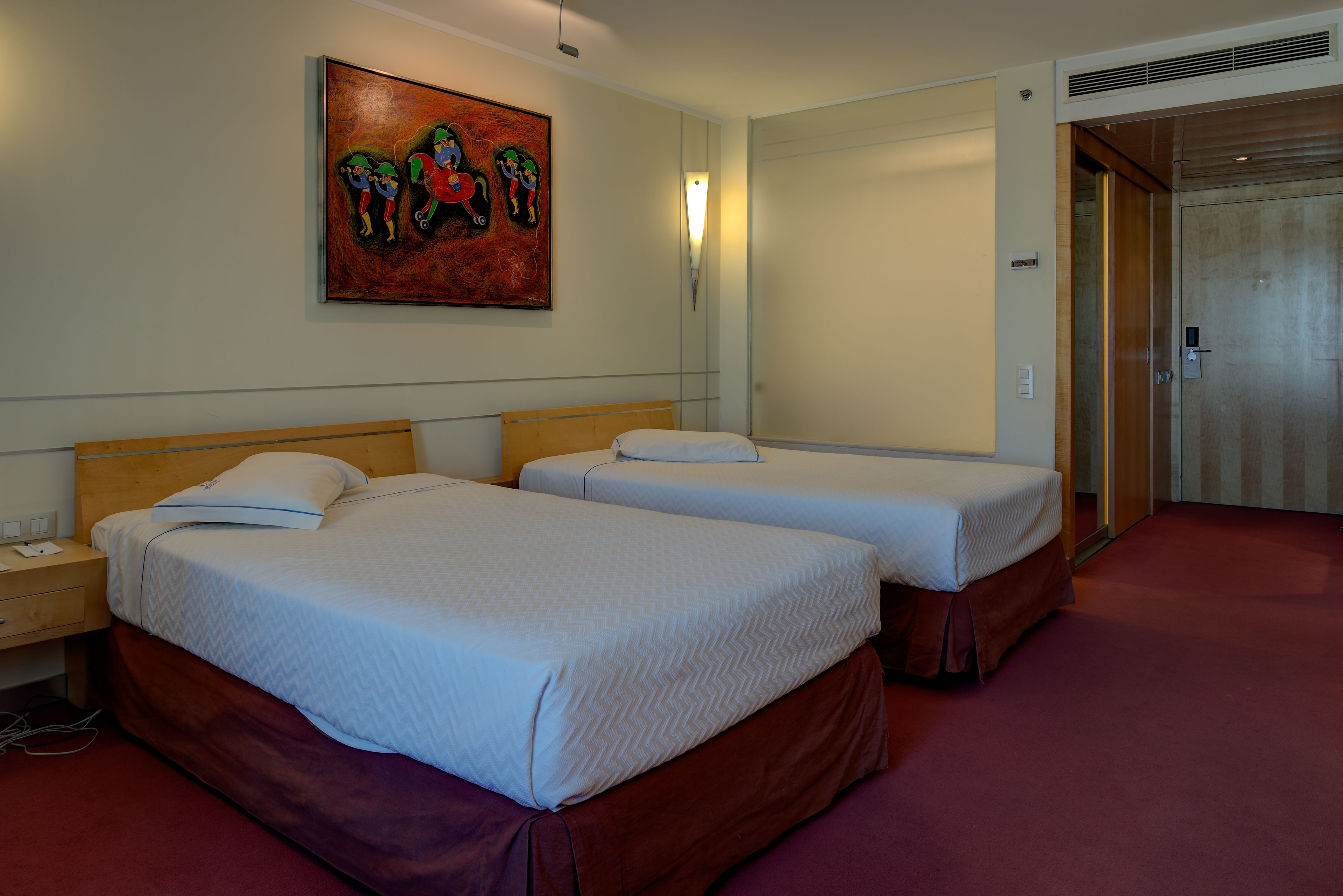 Een hotelkamer met twee bedden, een nachtkastje, een schilderij en een deur.