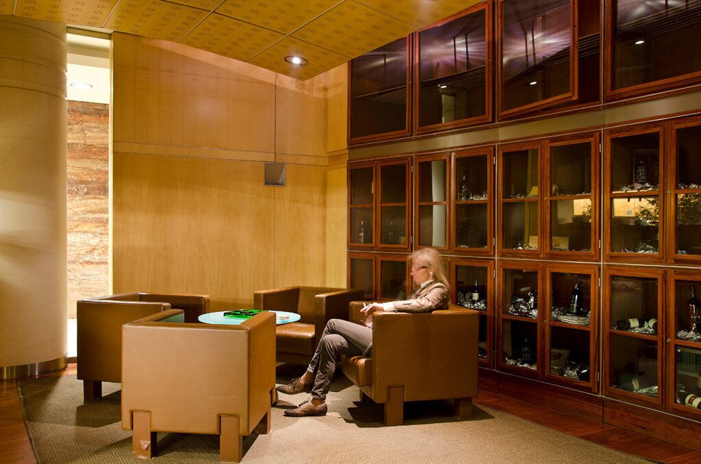 Una habitación con un armario de madera lleno de cristalería, una mesa redonda con sillas y una persona sentada.