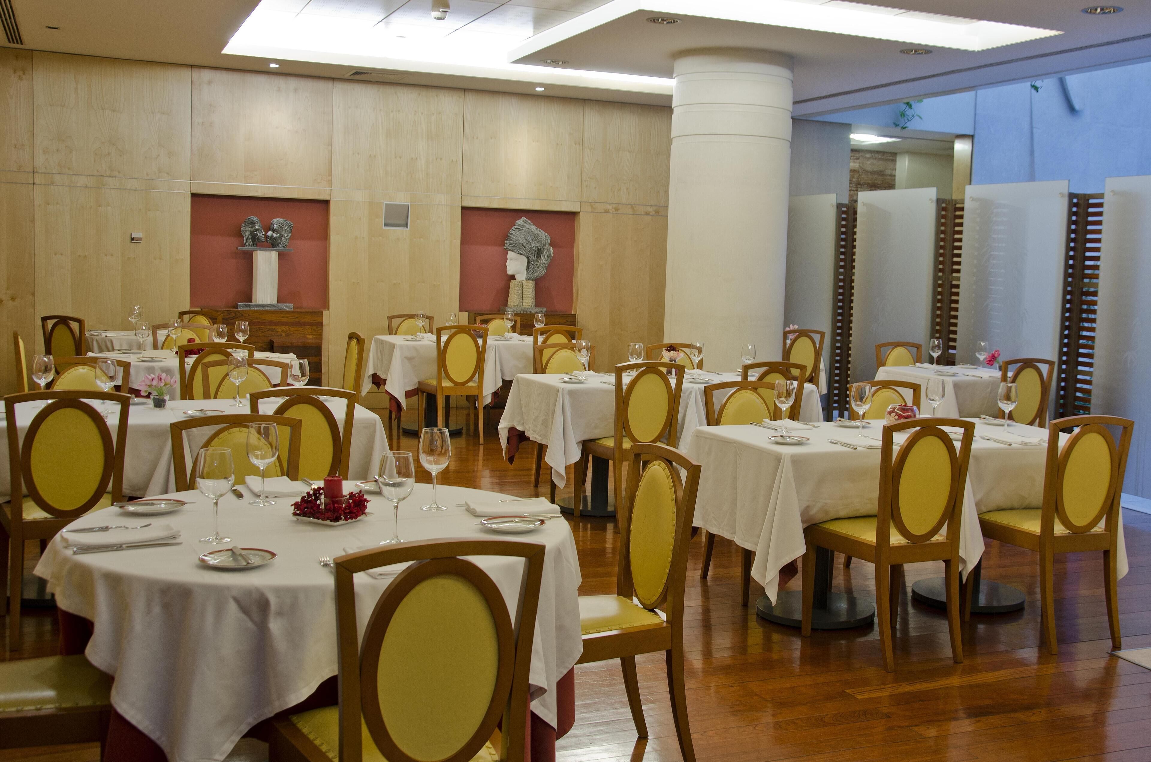 Comedor con mesas redondas, sillas amarillas y manteles blancos.