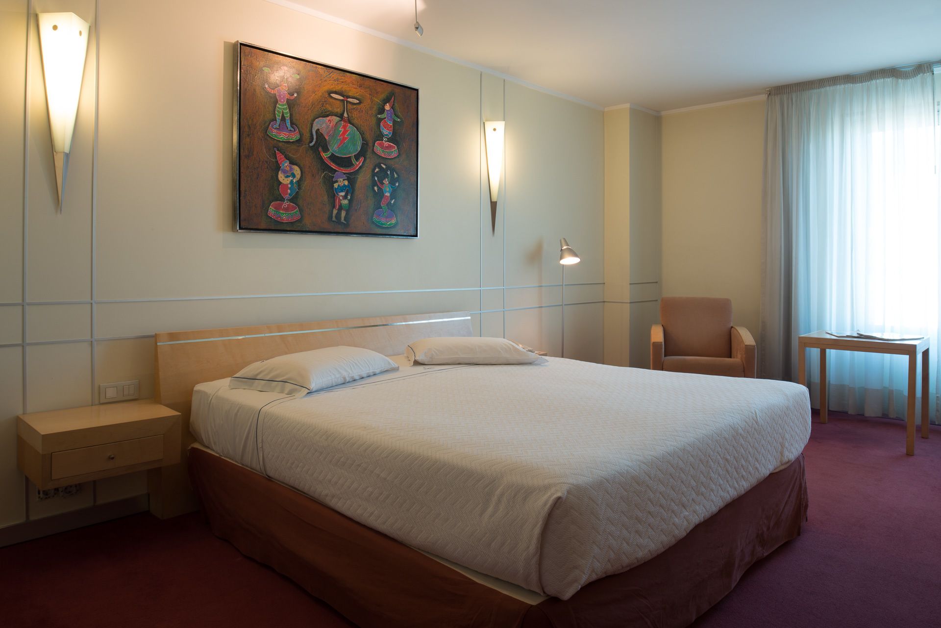 Habitación de hotel con una cama grande, una silla, un escritorio y un cuadro en la pared.