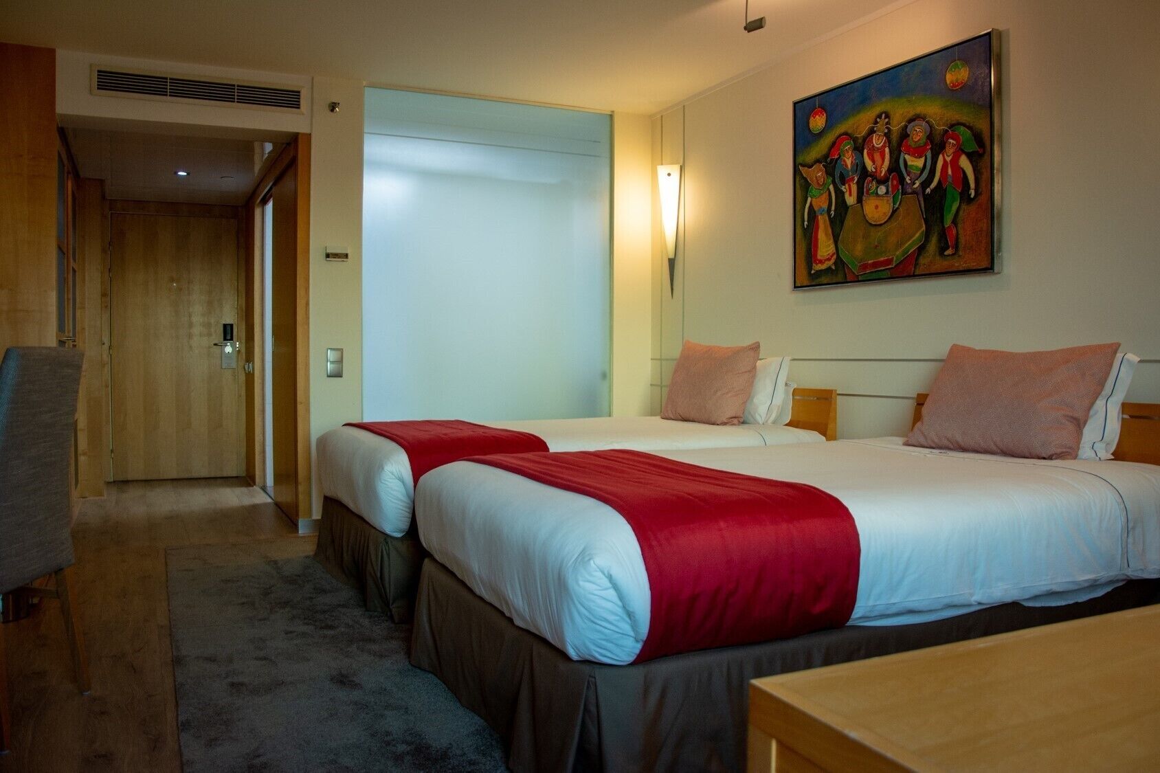 A hotel room with two beds, a painting on the wall, and a door leading to another room.