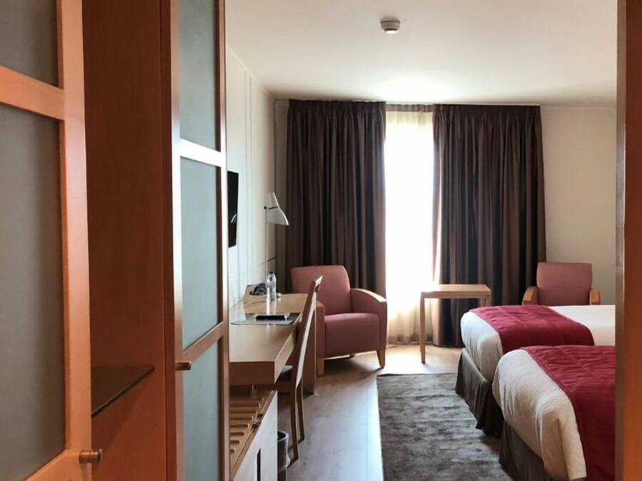 A hotel room with a desk, two chairs, a bed, and a small table.
