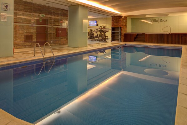 A swimming pool with clear water, a glass wall, and a TV screen in the background. - VIP Executive Entrecampos Hotel & Conference (Lisbon)
