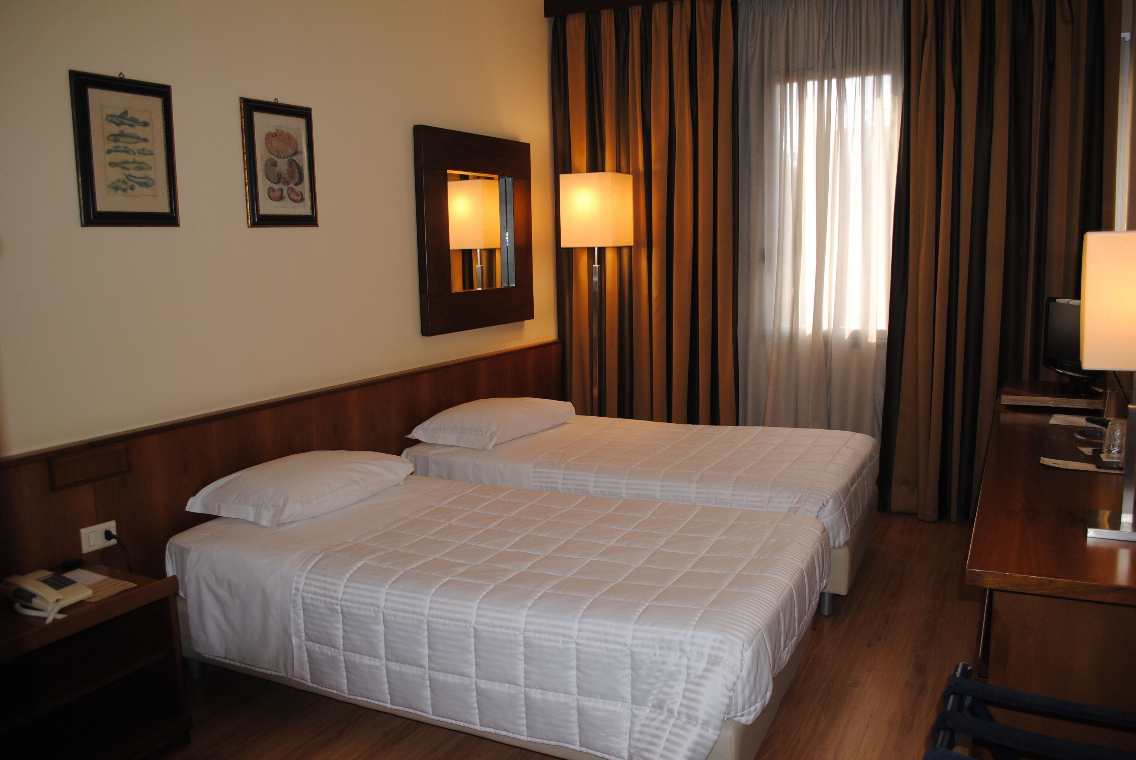 Una habitación de hotel con dos camas, un escritorio, una silla, una lámpara y un espejo.