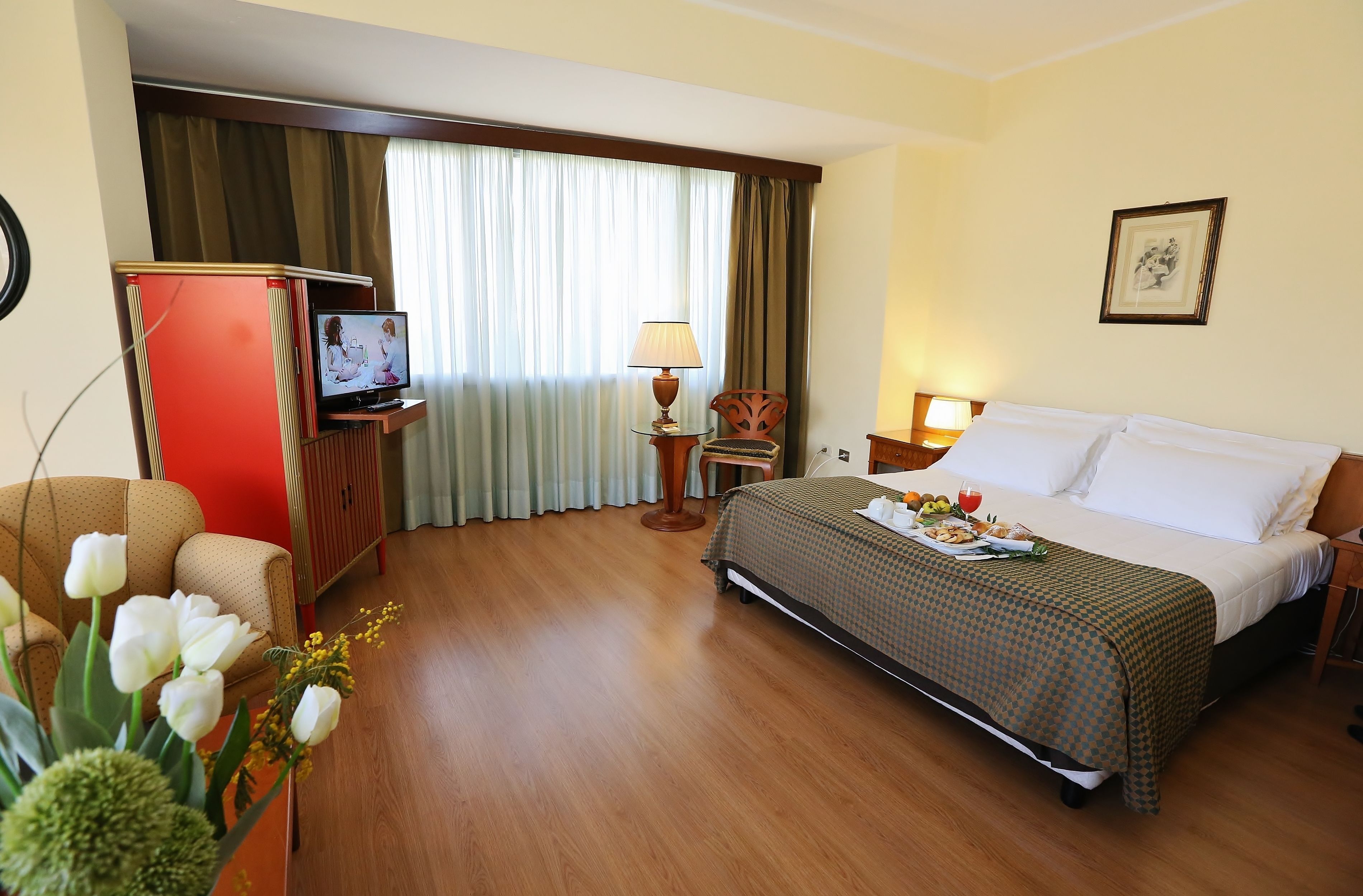 A hotel room with a bed, a TV, a desk, a chair, a lamp, and a picture on the wall.