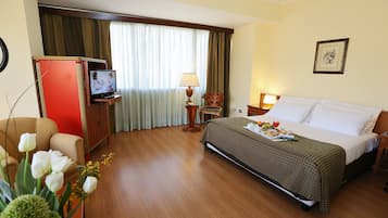 A hotel room with a bed, a TV, a desk, a chair, a lamp, and a picture on the wall.