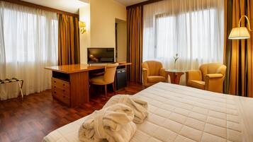 Una habitación de hotel con una cama, un escritorio con televisor, dos sillones y una lámpara.