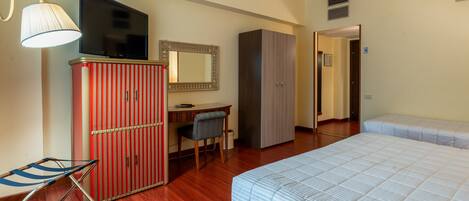 A hotel room with a bed, a desk, a chair, a wardrobe, a television, and a lamp.