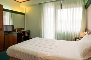 A hotel room with a bed, a desk with a computer, a mirror, and a window with curtains. - Hotel Royal Palace (Messina)