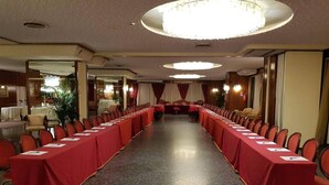 A long conference room with rows of tables and chairs, a chandelier, and a view of a hotel lobby.