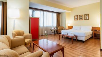 Una habitación de hotel con cama, dos sillones, una mesita, un escritorio y un armario rojo.