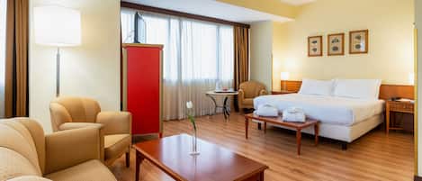 Una habitación de hotel con cama, dos sillones, una mesita, un escritorio y un armario rojo.