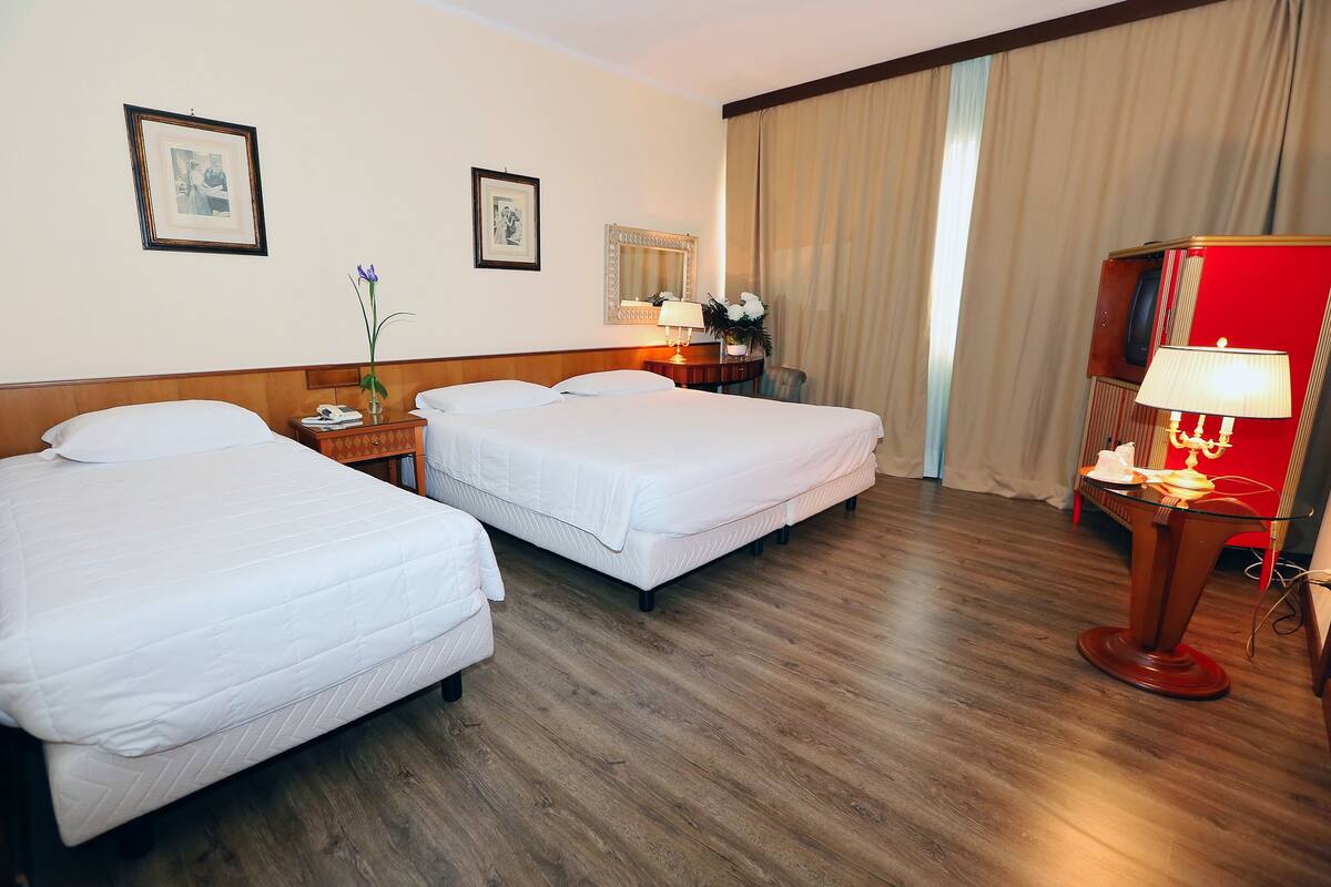 Une chambre d’hôtel avec deux lits, un plancher en bois, un bureau avec une lampe et une armoire rouge.