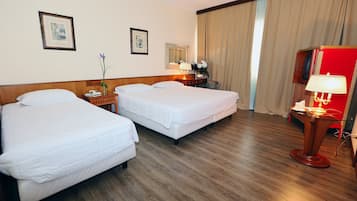 Ein Hotelzimmer mit zwei Betten, Holzboden, Schreibtisch mit Lampe und einem roten Schrank.