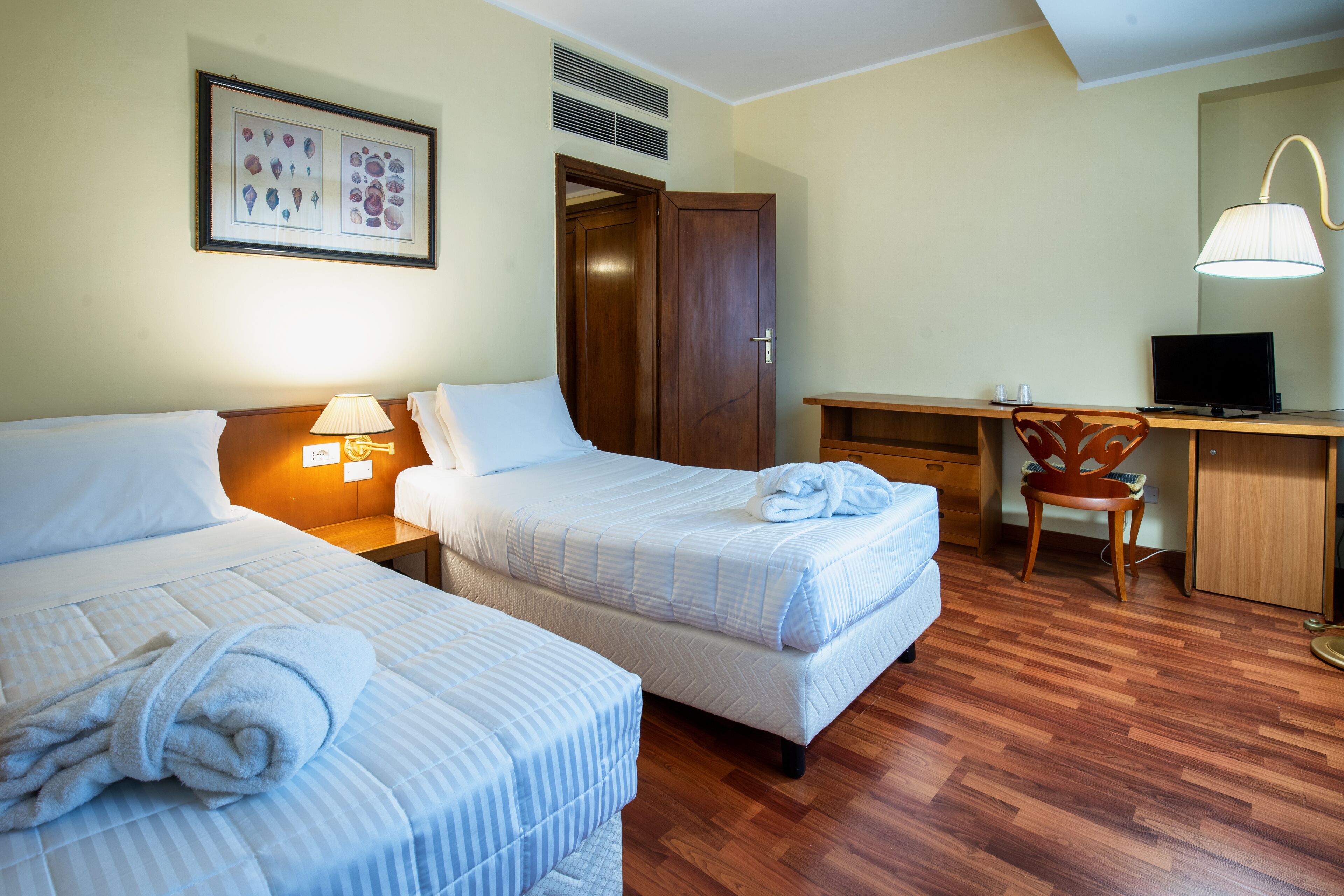 A hotel room with two beds, a desk, a chair, a TV, and a framed picture on the wall.
