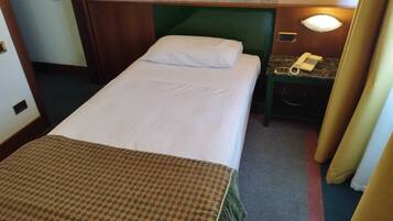 A hotel room with a single bed, a nightstand with a telephone, and a wall-mounted lamp.