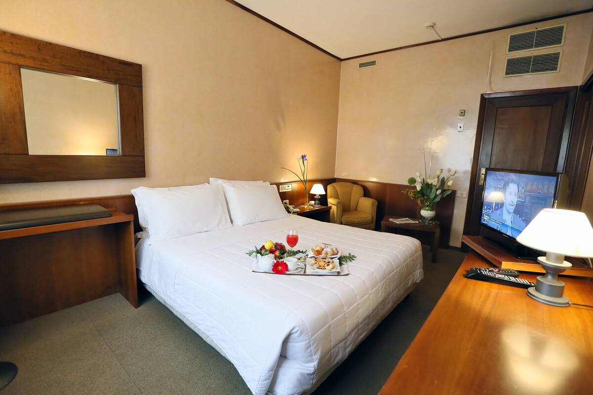 Une chambre d’hôtel équipée d’un lit, d’un bureau, d’une chaise, d’une télévision et d’une table de chevet avec une lampe.