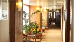 A hotel hallway with wooden walls, a carpeted floor, and several tables with chairs.