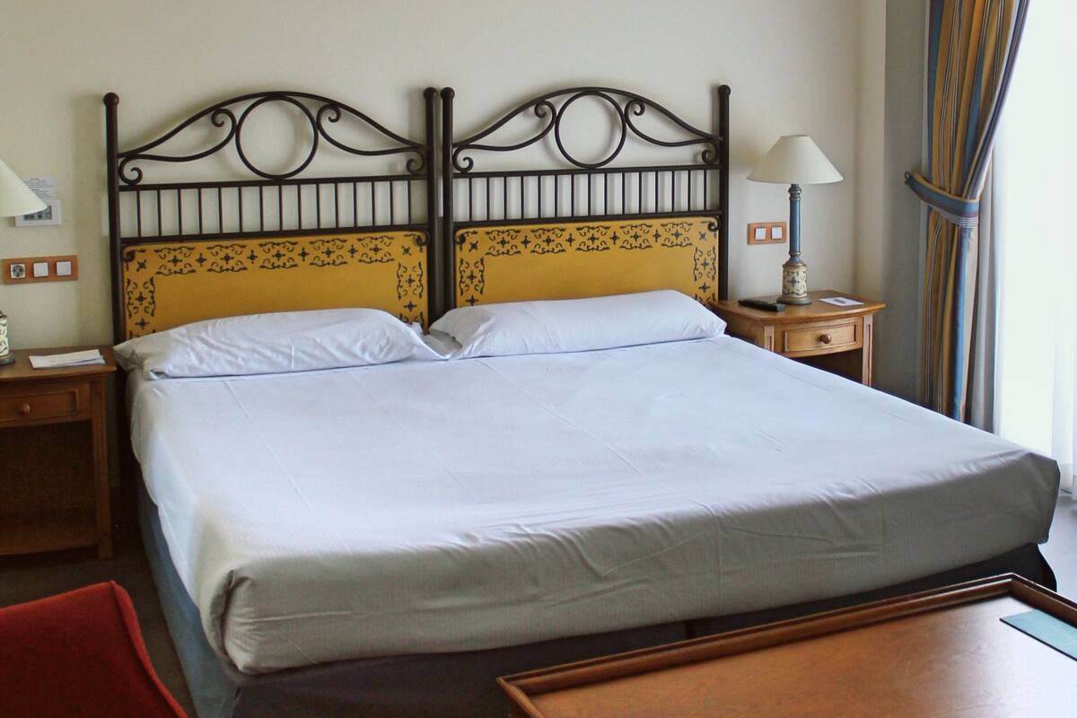 Habitación de hotel con cama doble, mesita de noche de madera con lámpara, una silla roja y una mesa de madera.