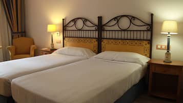 Habitación de hotel con dos camas individuales, una silla, dos mesitas de noche con lámparas y una cortina.