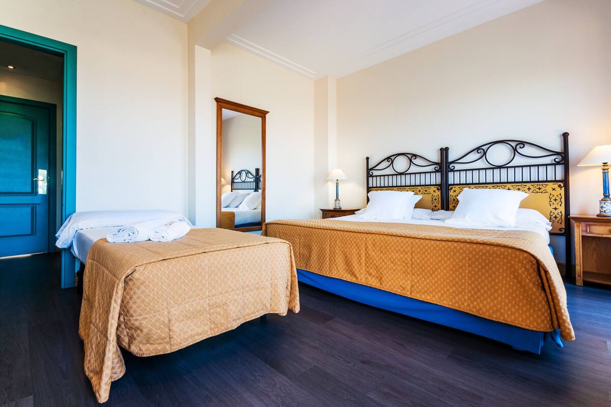 Una habitación de hotel con dos camas, un espejo grande y una mesita de noche con lámpara.