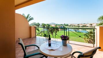A balcony with a table, chairs, a bottle of wine, and a potted plant.